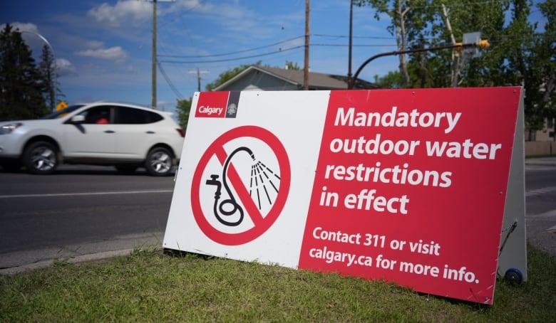 a sandwich board on the green grass reads "mandatory outdoor water restrictions in effect"
