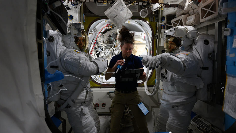 Three astronauts, two in spacesuits, test spacesuits for a spacewalk on the International Space Station.